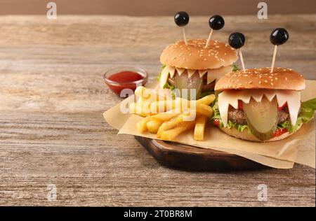 Niedliche Monster Burger serviert mit Pommes frites und Ketchup auf Holztisch, Platz für Text. Halloween Party Essen Stockfoto