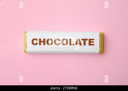 Ein Schokoladenriegel in der Verpackung auf rosa Hintergrund, Draufsicht Stockfoto
