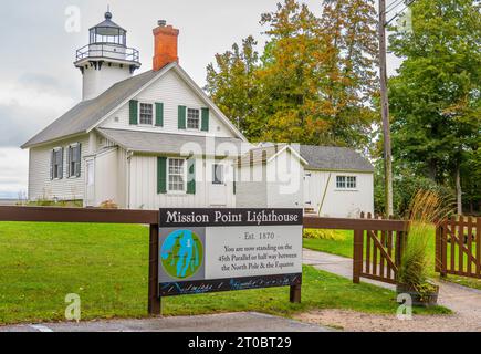 Mission Point Lighthouse befindet sich am 45. Breitengrad. Sie können sehen, wie das detaillierte Schild erklärt. Ein Zaun umgibt das alte weiße Gebäude mit grünen Fensterläden. Stockfoto