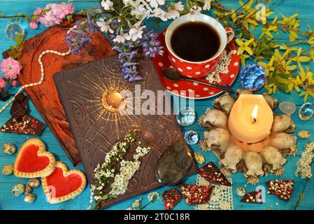 Magisches Zauberbuch mit Kerzen und einer Tasse Kaffee auf dem Ritualtisch. Okkultes, esoterisches und Wahrsagungsstilleben. Mystischer Hintergrund mit Vintage-Objekt Stockfoto