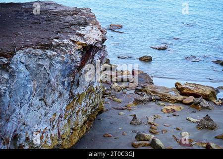 Eine wunderschöne mehrfarbige Gezeitenstrandklippe mit braunen, roten, orangen und weißen Farben, mit Blick auf das azurfarbene Meer. Stockfoto