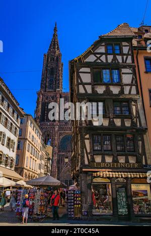 Straßburg, Frankreich - 31. Mai 2023: Fassade und Turm der Kathedrale Notre Dame und verzierte traditionelle Fachwerkhäuser mit steilen Dächern um sie herum Stockfoto