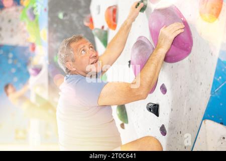 Der ältere Mann klettert ohne Seile und Gurte an der Boulderwand Stockfoto