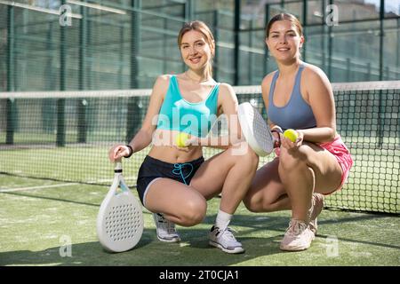 Junge Frauen posieren mit Padel-Schläger in den Händen neben dem Netz auf dem Tennisplatz Stockfoto