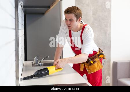 Junger gutaussehender Mann, der das Haus putzt. Attraktiver Typ, der einen Staubsauger in der Küche hält Stockfoto