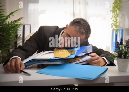 Geschäftsmann schläft vor Erschöpfung auf einem Stapel von Akten und Dokumenten auf dem Schreibtisch im Büro Stockfoto