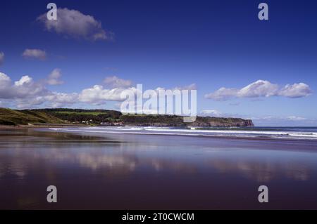 Blick auf Sandsend auf Strandhöhe vom Upgang Beach in Whitby an einem sonnigen Tag mit weißen Wolken, die sich im nassen Sand am Strand spiegeln. Stockfoto