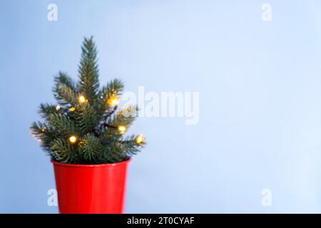 Verschwommener Weihnachtshintergrund. Weihnachtsbaum in einem roten Eimer mit Girlande mit Lichtern auf blauem Hintergrund, festliches goldenes Bokeh. Weihnachten und Winter Stockfoto