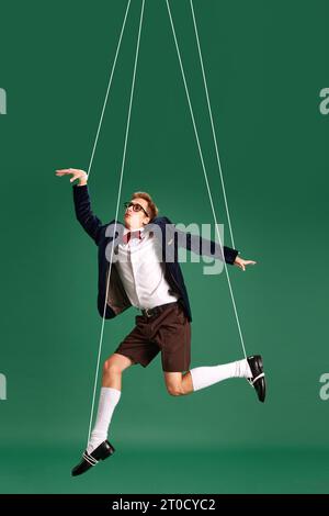 Junger Kerl, Marionette auf Schnur in Bewegung vor grünem Studiohintergrund. Puppe. Druck und Manipulation Stockfoto