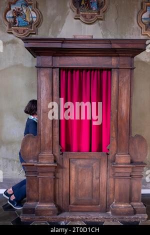 Frau gesteht in einer wunderschönen Kirche von San Carpoforo mit Sonnenlicht in Bissone, Tessin, Schweiz Stockfoto