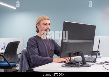 Porträt eines seriösen, eleganten, reifen Mannes, der auf einem Schreibtisch sitzt und einen Computer in einer Zusammenarbeit benutzt Stockfoto