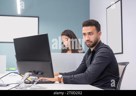 Porträt eines brünetten modernen und konzentrierten Mannes, der Computer benutzt, in einem Co-Working neben einer Frau Stockfoto