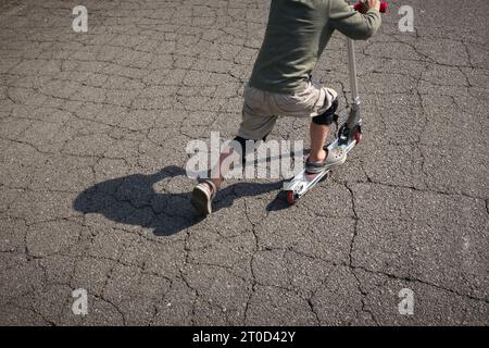 Junge, der Roller auf der Vorstadtstraße reitet. Stockfoto