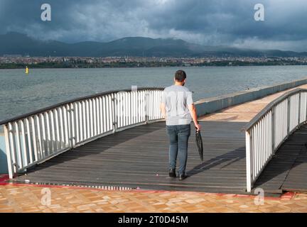 Degirmendere, Kocaeli, Türkei: Die ergreifende Reise der Einsamkeit, während ein einsamer und depressiver Mann im Regen mit einem Regenschirm in der Hand eine Brücke überquert Stockfoto