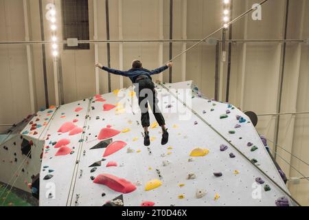 Junge, der sich von einer Kletterwand zurücklehnt, während er in einem Indoor-Fitnessstudio klettert Stockfoto