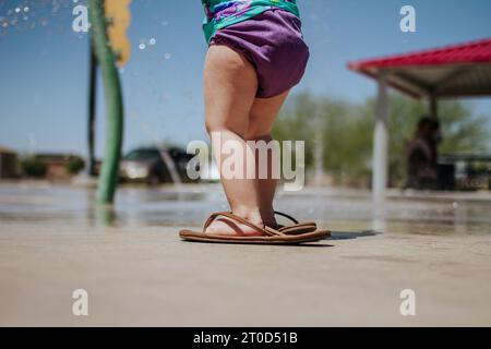 Ein Kleinkind trägt draußen Sandalen für Erwachsene Stockfoto