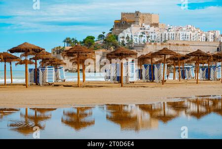 Ein Blick auf die Altstadt von Peniscola, Spanien, mit seiner Burg auf der Spitze, vom Norte-Strand aus gesehen, mit einigen einsamen rustikalen Sonnenschirmen im Nebel Stockfoto