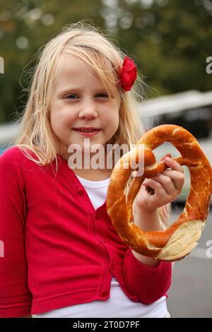 Glückliches blondes Mädchen, das Brezel hält, traditionelles bayerisches Essen Stockfoto