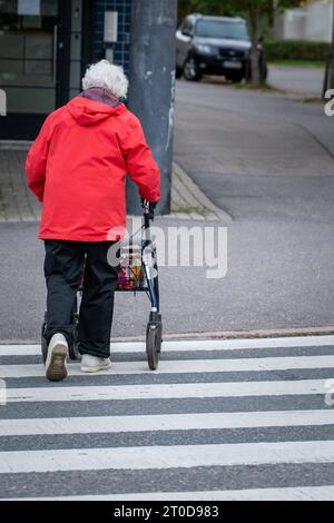 Eine ältere Frau, die mit einem Rollator auf den Straßen der Stadt läuft Stockfoto