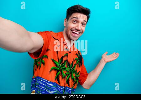 Porträt des lustigen Mannes mit Borsten tragen tropisches Hemd Palme demonstrieren Objekt leeren Raum auf Selfie isoliert auf blauem Hintergrund Stockfoto