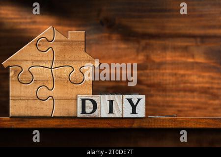 Holzhaus aus Puzzleteilen und Text DIY (Do it yourself), aus Holzblöcken, auf einer Holzwerkbank mit Kopierraum. Stockfoto