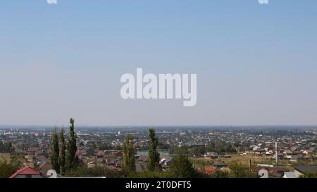 Blick auf eine südliche Stadt von einem Hügel mit vielen kleinen Gebäuden und hohen Bäumen an einem sonnigen, klaren Sommertag, eine Stadtlandschaft in der Ferne Stockfoto
