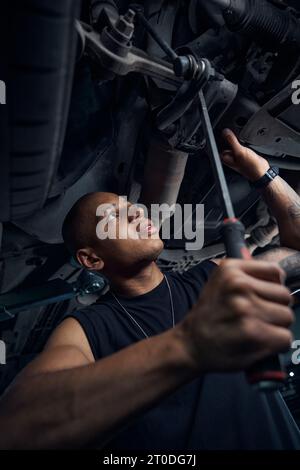 Fokussierter afroamerikanischer Automechaniker, der die Integrität von Autoachsen und -Hebeln überprüft Stockfoto