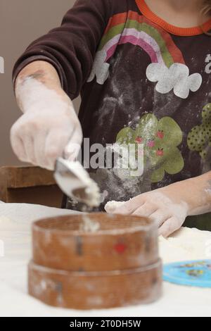 Eine Frau, die in heller Kleidung verziert ist, kreiert geschickt aus Teig in ihrem Haus ein künstlerisches Meisterwerk, schneidet und formt mit präzisen Bewegungen Stockfoto