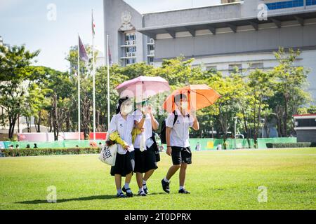 Thailändische Universitätsstudenten schlendern über den Hauptrasen der Srinakharinwirot University Bangkok, Thailand, und werden von Gartenregnern nass. Stockfoto