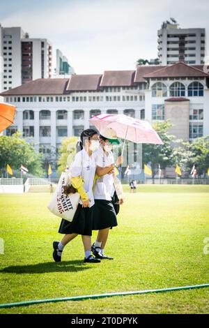 Thailändische Universitätsstudenten schlendern über den Hauptrasen der Srinakharinwirot University Bangkok, Thailand, und werden von Gartenregnern nass. Stockfoto