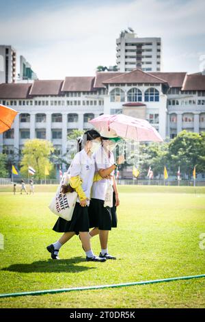 Thailändische Universitätsstudenten schlendern über den Hauptrasen der Srinakharinwirot University Bangkok, Thailand, und werden von Gartenregnern nass. Stockfoto