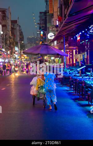 Vietnamesische Street Food-Verkäuferin schiebt ihren Wagen die Bui Vien Walking Street in Night, Ho Chi Minh City, Vietnam Stockfoto