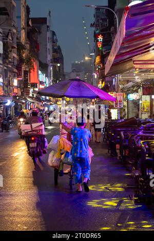 Vietnamesische Street Food-Verkäuferin schiebt ihren Wagen die Bui Vien Walking Street in Night, Ho Chi Minh City, Vietnam Stockfoto