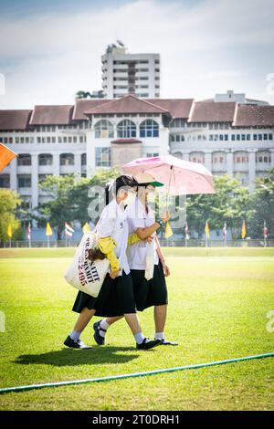 Thailändische Universitätsstudenten schlendern über den Hauptrasen der Srinakharinwirot University Bangkok, Thailand, und werden von Gartenregnern nass. Stockfoto