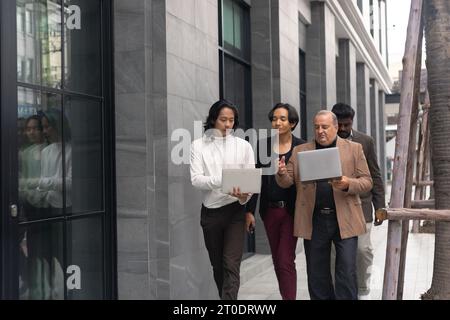 Besprechung des Geschäftsteams. Eine Gruppe von Diversity-Geschäftsleuten spricht Kollegen, während sie gegen zeitgenössische Firmengebäude in der Stadt laufen. Stockfoto