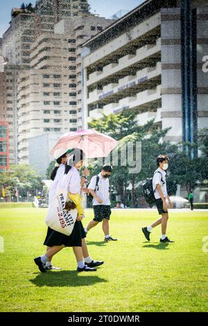 Thailändische Universitätsstudenten schlendern über den Hauptrasen der Srinakharinwirot University Bangkok, Thailand, und werden von Gartenregnern nass. Stockfoto