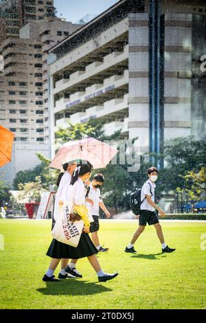 Thailändische Universitätsstudenten schlendern über den Hauptrasen der Srinakharinwirot University Bangkok, Thailand, und werden von Gartenregnern nass. Stockfoto