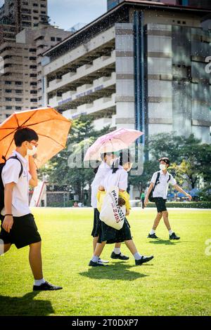 Thailändische Universitätsstudenten schlendern über den Hauptrasen der Srinakharinwirot University Bangkok, Thailand, und werden von Gartenregnern nass. Stockfoto