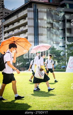 Thailändische Universitätsstudenten schlendern über den Hauptrasen der Srinakharinwirot University Bangkok, Thailand, und werden von Gartenregnern nass. Stockfoto