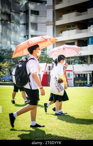 Thailändische Universitätsstudenten schlendern über den Hauptrasen der Srinakharinwirot University Bangkok, Thailand, und werden von Gartenregnern nass. Stockfoto