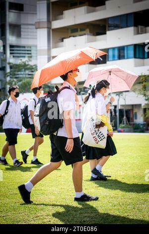 Thailändische Universitätsstudenten schlendern über den Hauptrasen der Srinakharinwirot University Bangkok, Thailand, und werden von Gartenregnern nass. Stockfoto