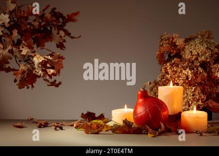 Stillleben mit Kürbis, ausgetrockneten Blättern und brennenden Kerzen. Im Hintergrund getrocknete Hortensienblüten und Eichenzweige. Herbstkonzept. Stockfoto