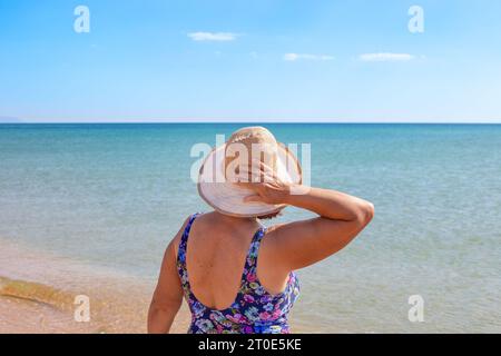 Eine Dame mit Hut und Badeanzug ruht an einem sonnigen Sommertag am Meer. Stockfoto