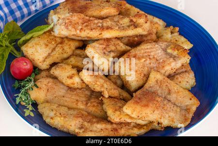 Knusprige frittierte Fischstücke auf einer blauen Platte auf dunklem Hintergrund, leckerer, gesunder und zufriedenstellender Teller. Stockfoto