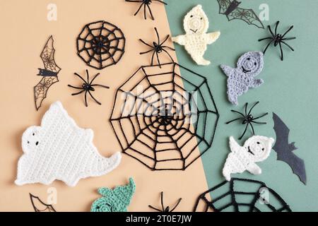 Halloween-Dekorationen, Geist, Spinnen, Fledermäuse, gestrickte Webs auf grünem und beigem Hintergrund. Flache Lage, Draufsicht Stockfoto