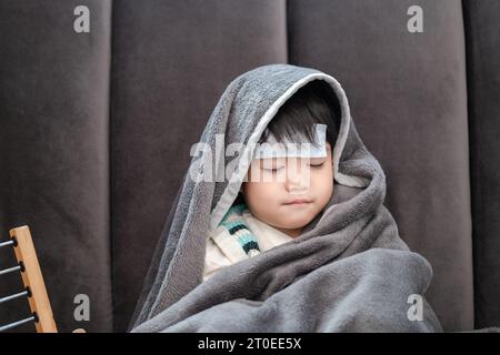 Der asiatische Junge lag krank, er hatte einen fiebersenkenden Fleck auf der Stirn und bedeckte sich wegen der Kälte mit einer Decke. Stockfoto