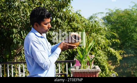 Attraktiver junger Mann auf Apartment Balcony Bewässerungspflanzen in Topf aus Kupfer kalash. Konzept „Baumstruktur speichern“. Stockfoto