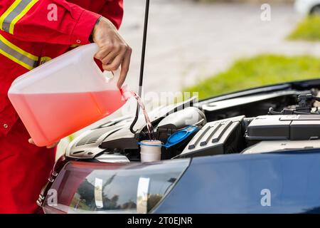 Nahaufnahme-Servicearbeiter, Fahrer, der aus der Aktivkohleflasche nicht gefrorene Scheibenwaschflüssigkeit in den Motorhaubentank gießt. Sommer- oder Winterflüssigkeit Scheibenreiniger für Flüssigglas Stockfoto