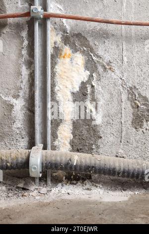 Nahaufnahme eines aktiven Wasserlecks in der Wand des Elektroraums oder Untergeschosses Feuchte dunkle Flecken mit weißer Fleckenbildung und Ausblendung über großen Elektrokabeln. Stockfoto