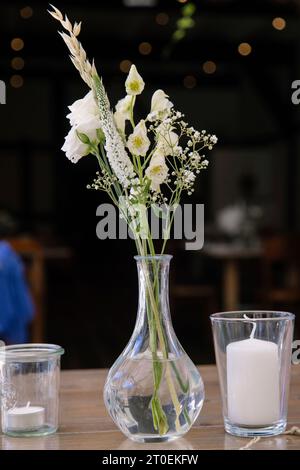 Kleine Glasvase mit weißen Blumen auf einem Holztisch Stockfoto